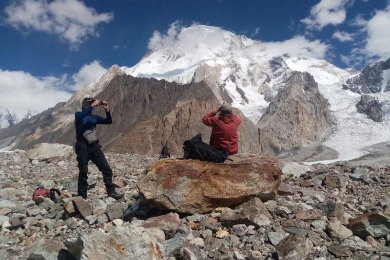 Two trekkers on the moraine photographing the face from a boulder