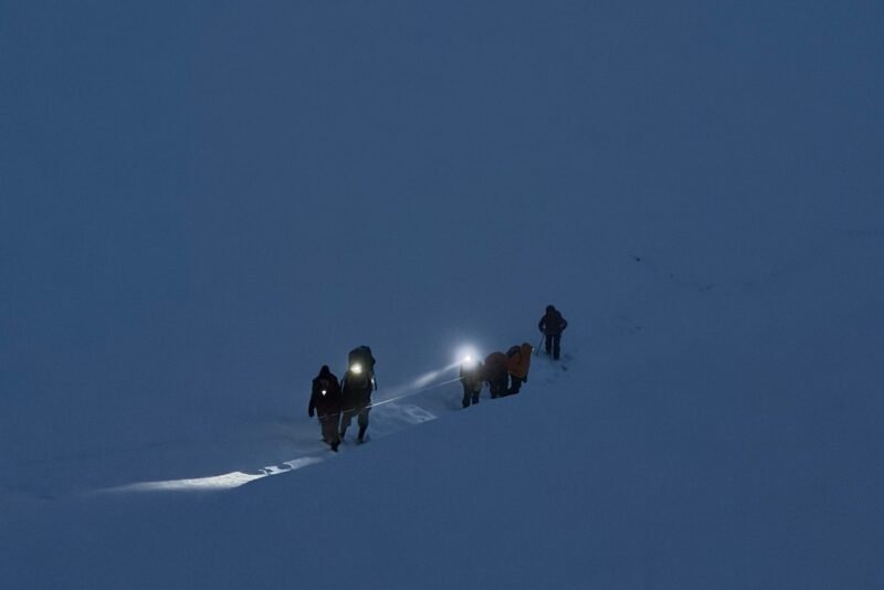 Climbers moving roped across snow before dawn, one headlamp lit, on the way to the pass