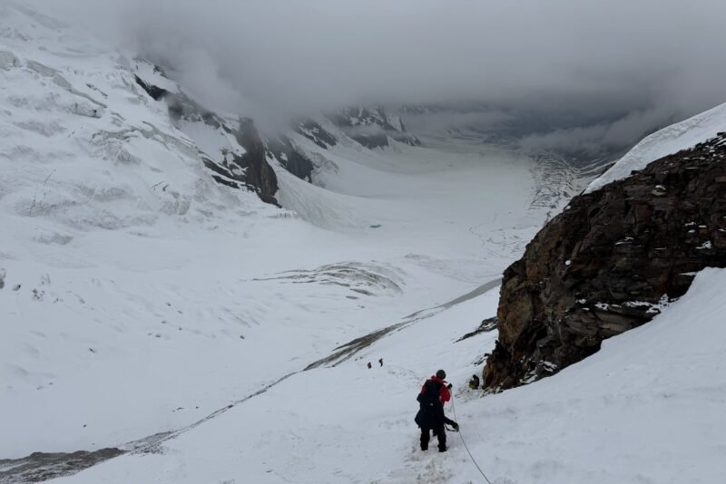 A climber on the glacier below the rock buttress, the scale of the basin behind