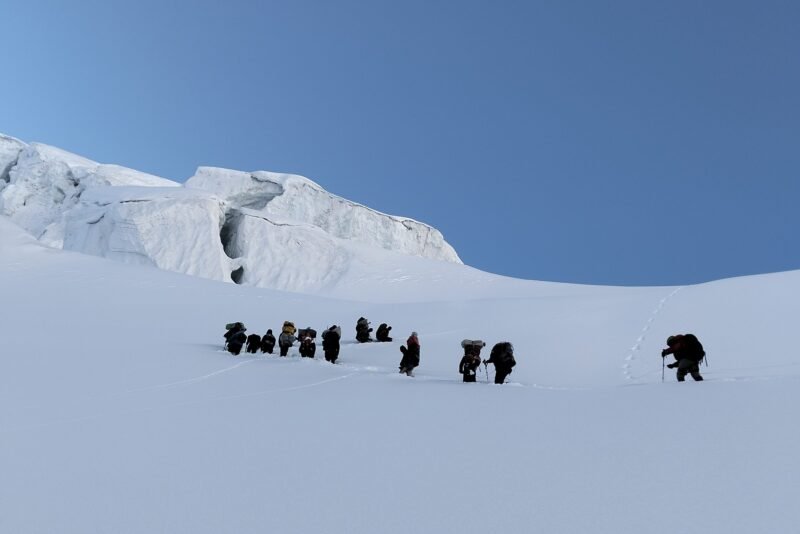 A line of climbers moving in single file across the snow basin, tracks behind them