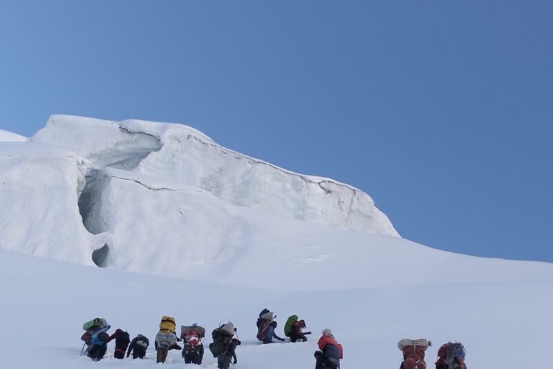 The group resting on the snow slope below the serac, packs and jackets on