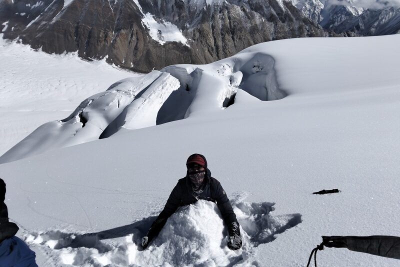 A climber in a snow hollow with equipment laid out beside them on the glacier